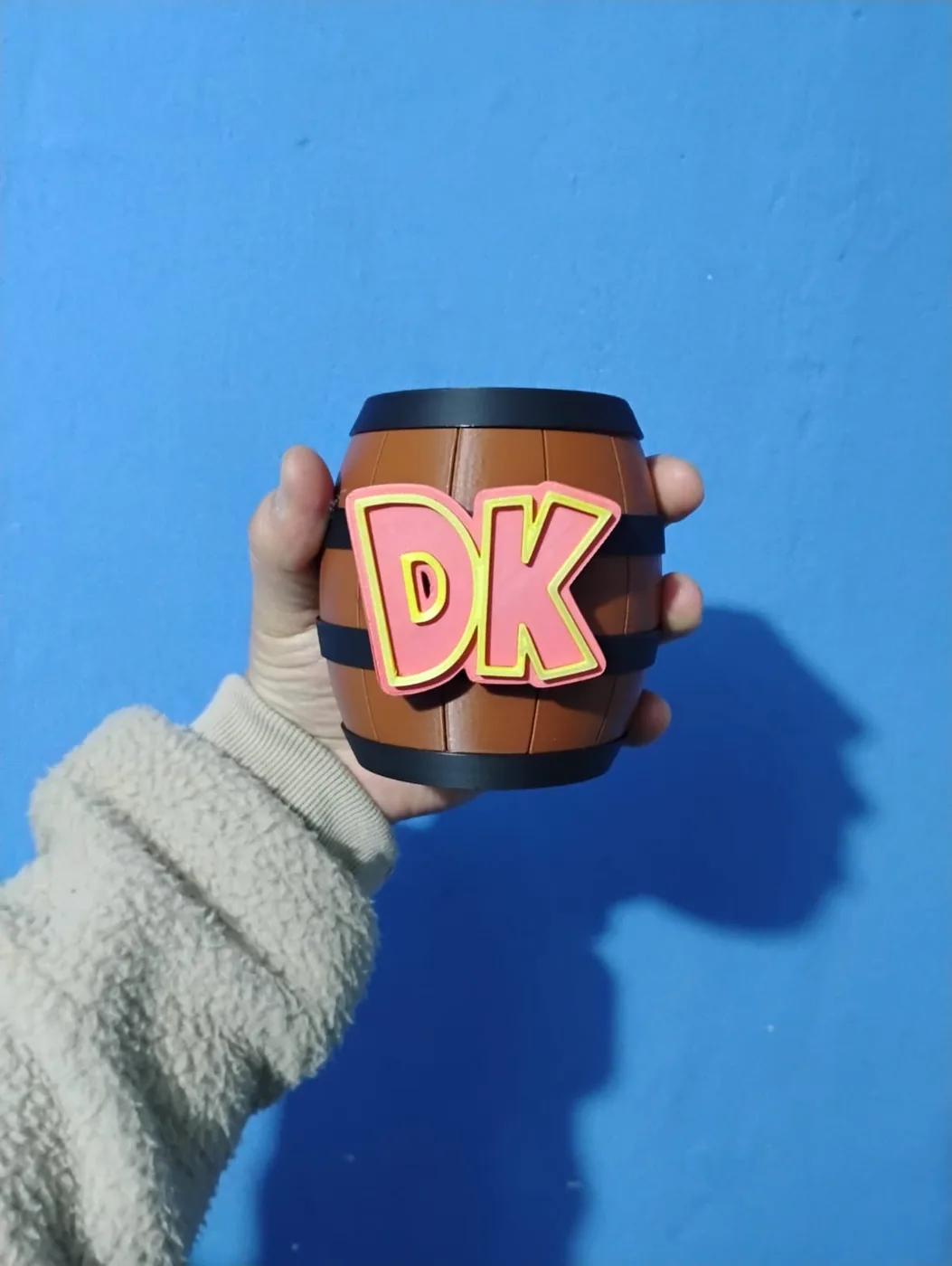 Barril café con las letras DK en relieve, sostenido en una mano