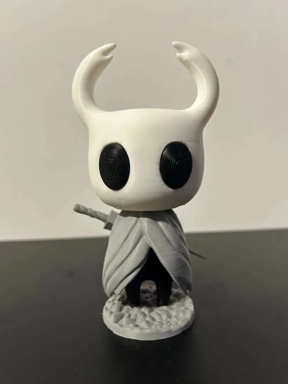 Figura del personaje de Hollow Knight en blanco y gris, con su aguijón